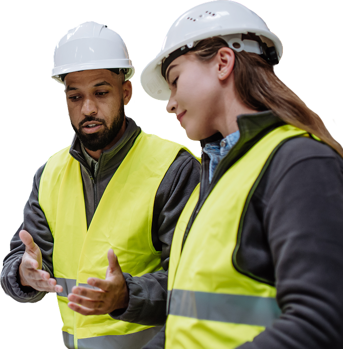 Two construction workers wearing yellow safety vests and white helmets discuss a project.