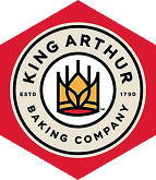 Logo of King Arthur Baking Company featuring a wheat emblem inside a circle with text, set against a red hexagonal background.